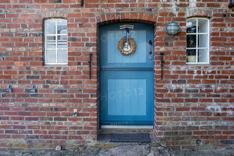 Blue wooden door in red brick wall with two windows and decorations, Föhr, Nordfriesland, Schleswig-Holstein, Germany, Europe