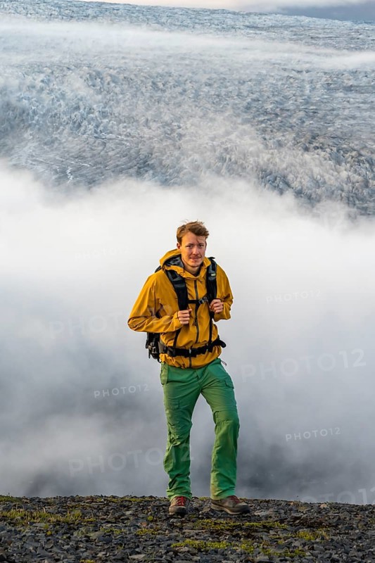 Young man in front of impressive landscape at sunset, fog, clouds moving around, glacier ice of the glacier tongue Kötlujökull, glacier Myrdalsjökull, Pakgil, Iceland, Europe