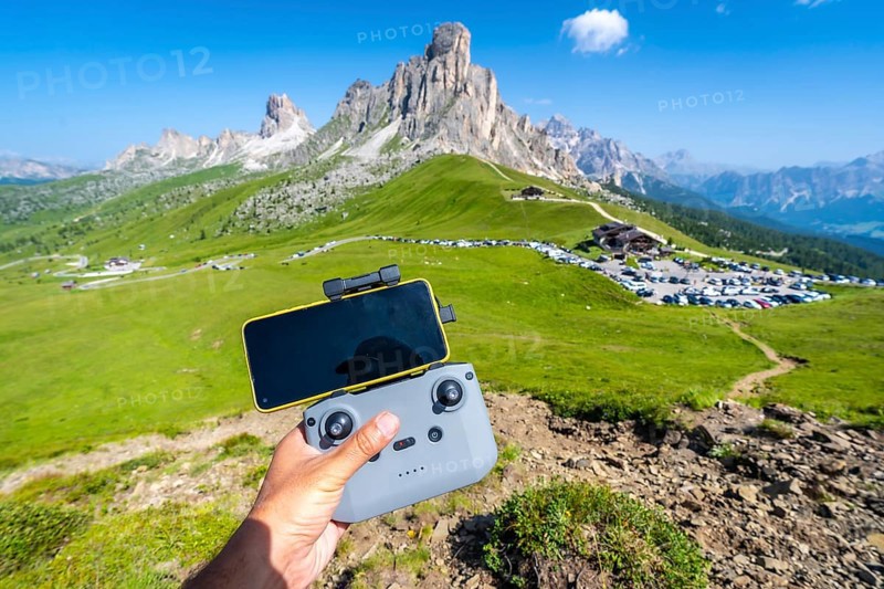 Hand piloting a drone with a smartphone attached to the controller in the scenic landscape of giau pass, dolomites, italy, during a sunny summer day