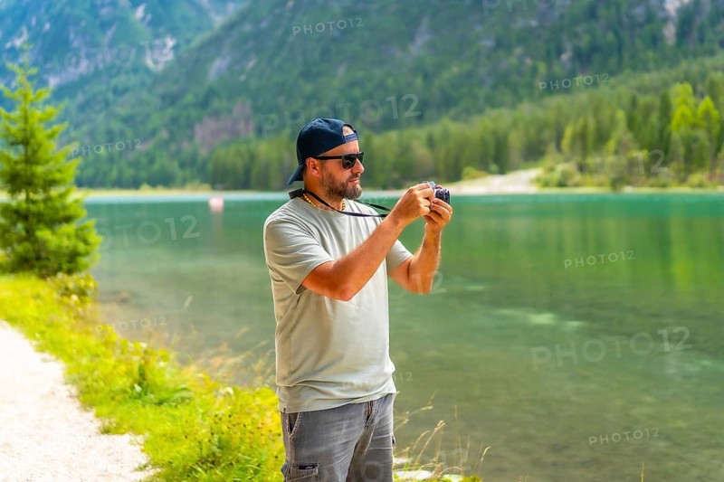 Tourist taking photos of the landscape at lake dobbiaco during summer holidays in the italian dolomites