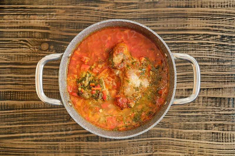 A hearty turkey stew with vibrant vegetables is simmering in a pot on a wooden surface. The rich red broth and tender meat suggest a comforting meal perfect for a gathering on a cozy day.