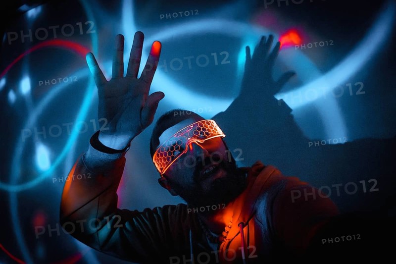 Cyberpunk man wearing illuminated goggles interacting with virtual reality game using augmented reality technology