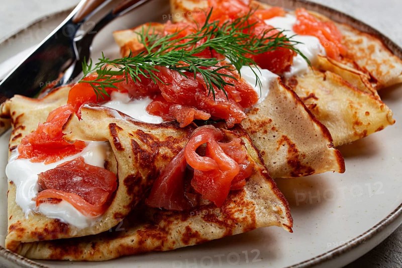 Delicious pancakes with salmon and sour cream, breakfast, on a plate, rustic style, with cutlery