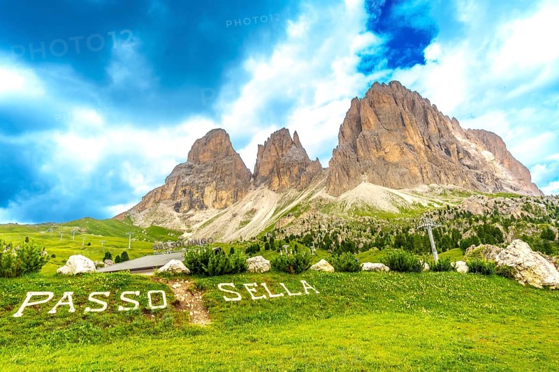 Green meadow with passo sella sign and the sassolungo group in the background, dolomites, italy