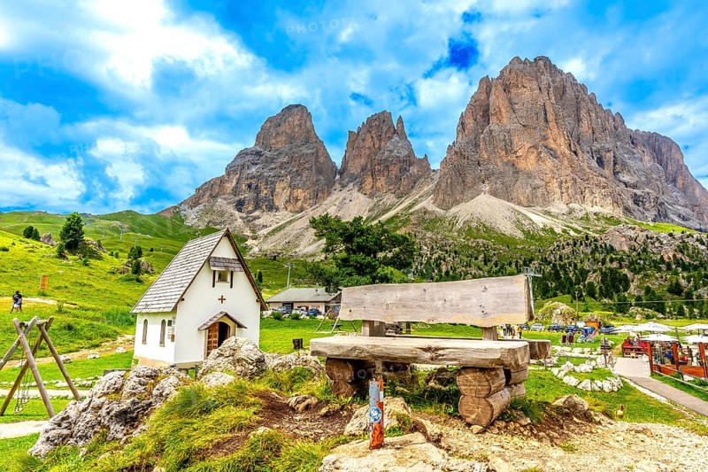 Breathtaking summer view of the majestic sassolungo mountain at sella pass, featuring a wooden bench and a small church in the dolomites, italy