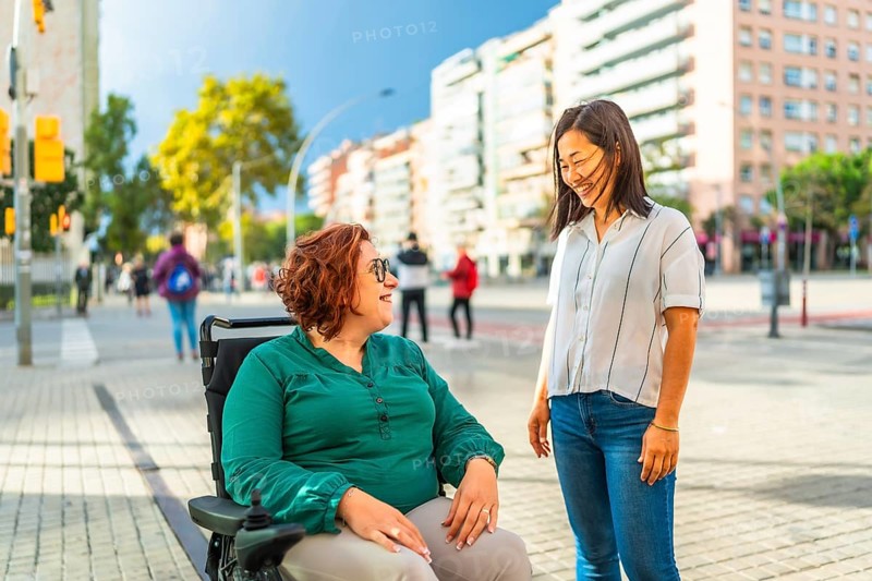 Woman with disabilities and asian caregiver talking relaxed in the city