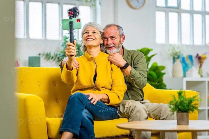 Happy senior couple during online meeting with the family using smartphone sitting on the sofa