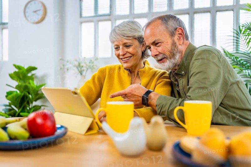 Senior man pointing the screen of a digital tablet with his wife aside