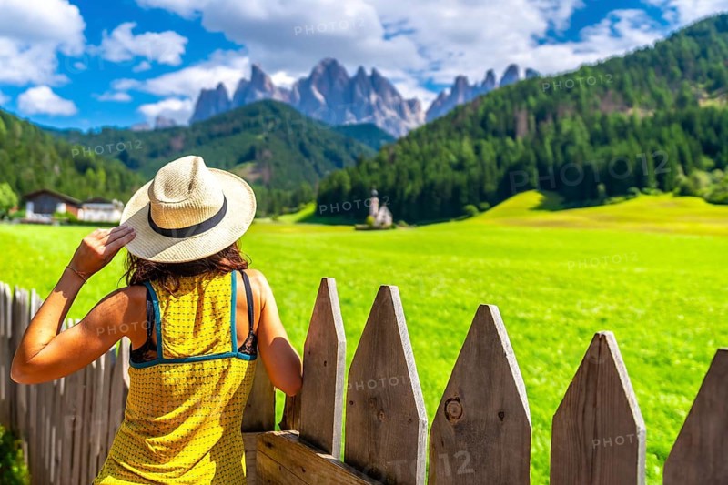 Female tourist wearing a straw hat admiring the stunning view of the odle mountains and st. Magdalena church in val di funes