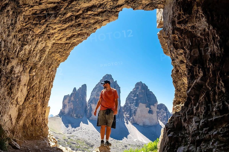 Hiker enjoying the scenic view of tre cime di lavaredo, a symbol of the dolomites, from inside a mountain Tre Cime Cave during a summer hike
