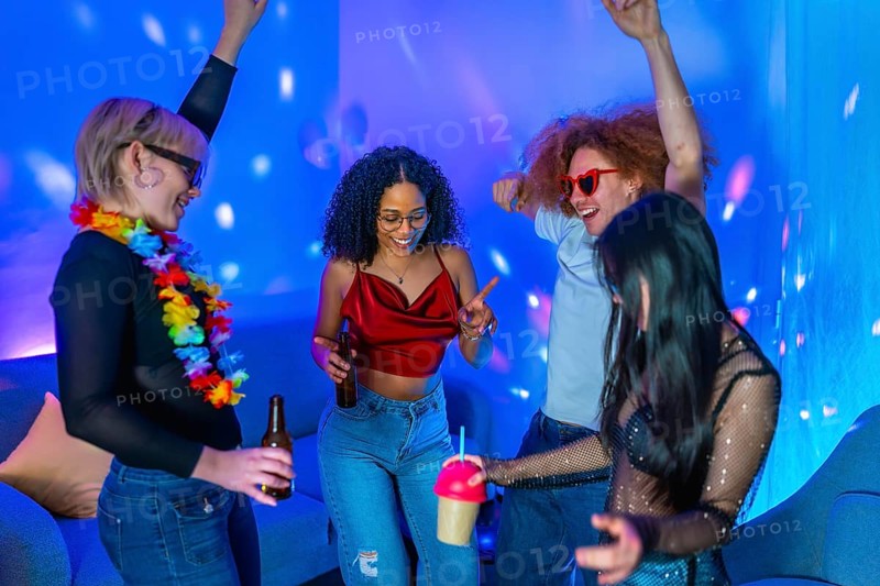 Cheerful multi ethnic friends dancing together and enjoying drinks at a home disco party with blue and pink lighting