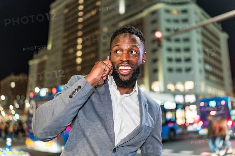 Young businessman engaging in a phone conversation while navigating the bustling city center at night, surrounded by vibrant lights and modern skyscrapers