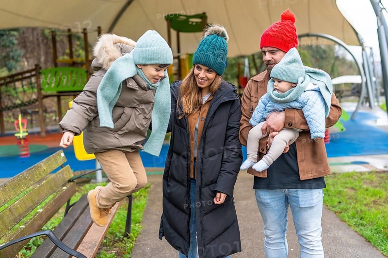Smiling family enjoying a joyful winter day at the playground, with children happily jumping on a bench and playing together