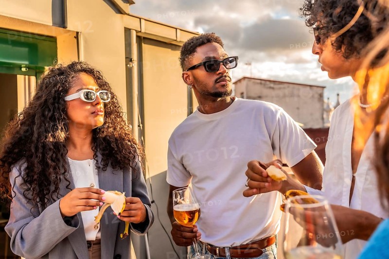 Multi-ethnic modern friends talking in a rooftop while drinking wine and eating snacks