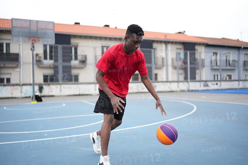 Full length photo of a sportive young african man dribbling at a basketball court