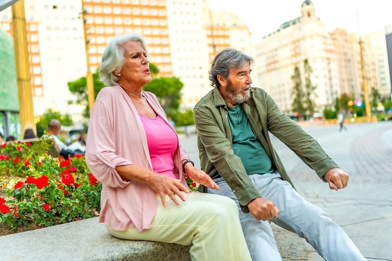 Senior couple of tourists resting on bench with tired expression in the city