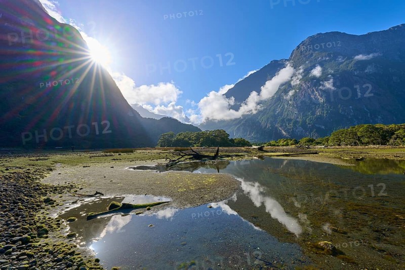 Dramatic sunbeams over mountains with clouds and water reflection, summer, Milford Sound, Te Anau, Fiordland National Park, South Island, New Zealand, Oceania
