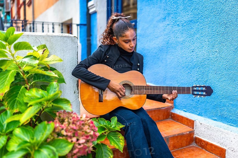 African american young beauty woman playing acoustic guitar outside a colorful house