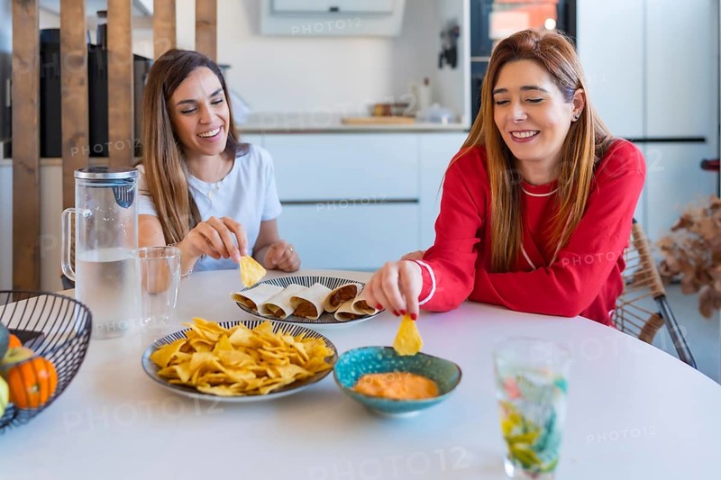 Two cheerful women enjoying a meal of quesadillas, nachos and sauce, creating a cozy and joyful atmosphere