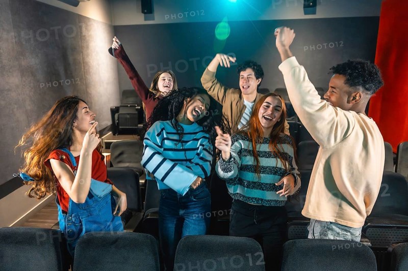 Cheerful multi ethnic friends dancing and enjoying music during movie disco event in cinema theater