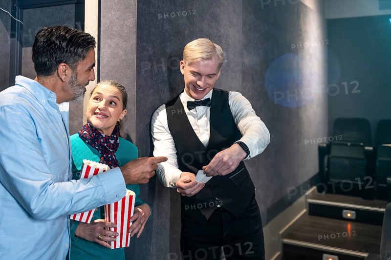 Couple holding popcorn buckets showing their tickets to the usher before entering the movie theater