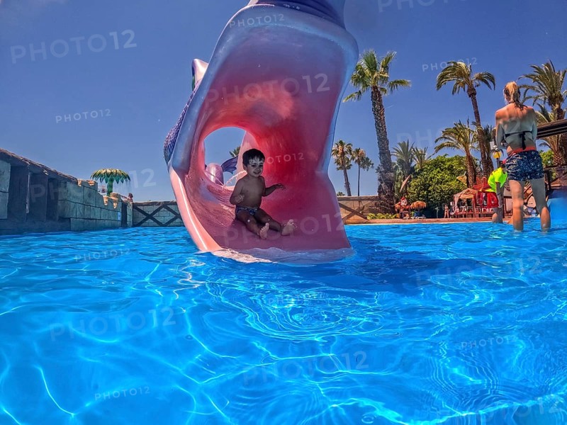 Young boy enjoying summer vacation sliding down a waterslide shaped like a monster's mouth into a refreshing blue pool