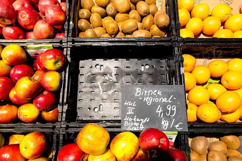 Fruit counter in a supermarket or organic food shop, here with different types of apples, kiwis, oranges and an empty compartment for pears