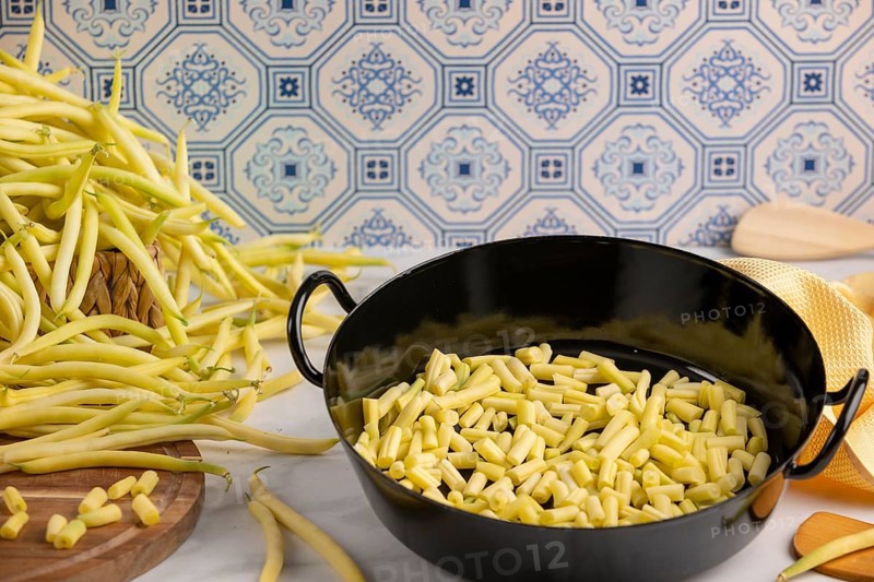 A cooking pot full of sliced beans on a kitchen worktop, whole runner beans in the background
