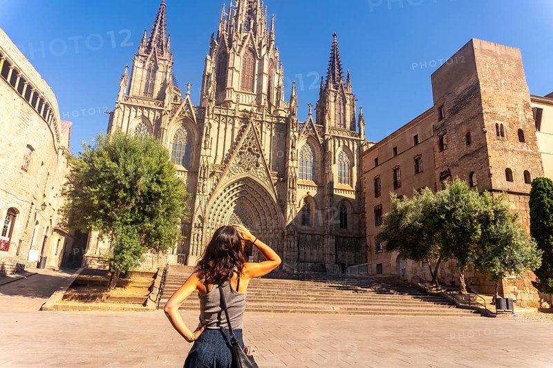 Young woman shielding her eyes from the sun while contemplating the majestic barcelona cathedral in the gothic quarter during a summer vacation