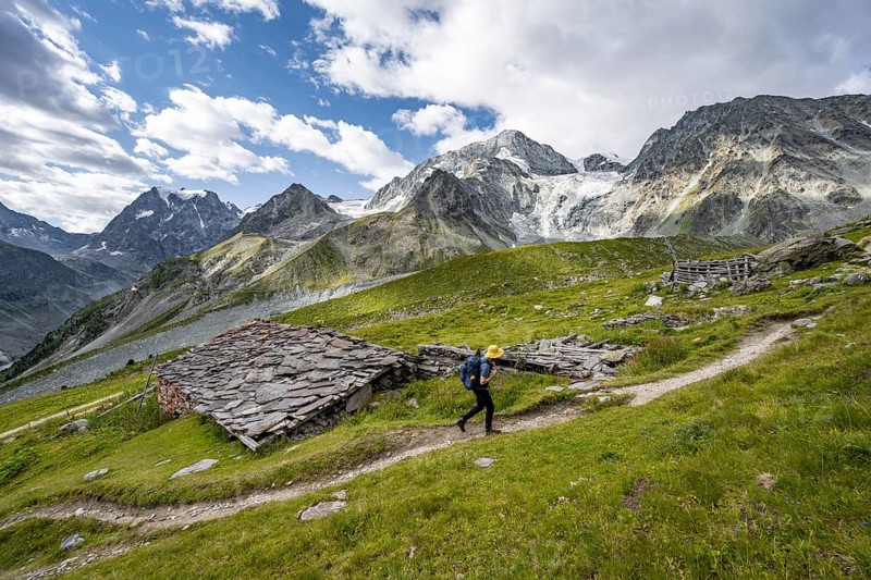 Mountaineers on a hiking trail, Alpine huts covered with slate slabs, mountain landscape near Arolla, behind mountain peak Mont Collon and glacier Glacier de Tsijore Nouve, Valais, Western Alps Switzerland