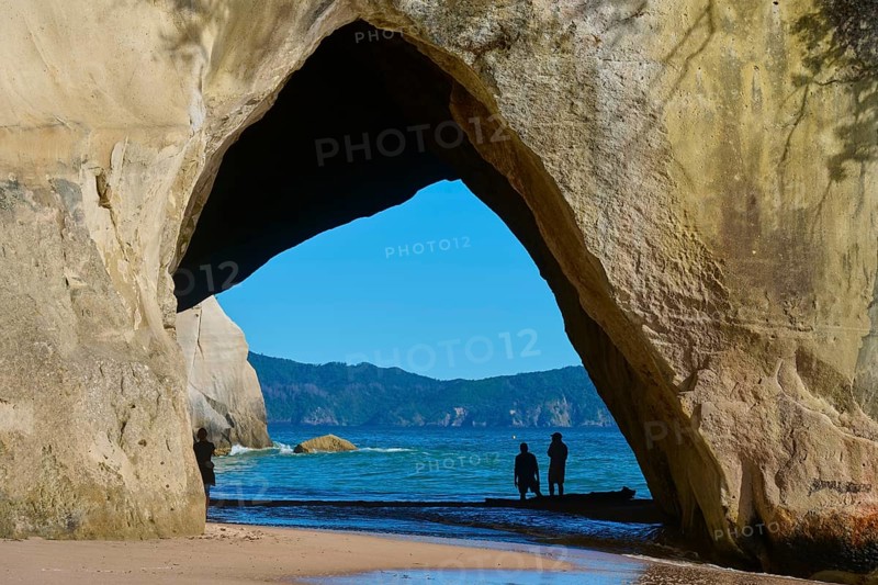 Silhouettes of people under a large rock arch on the beach overlooking the sea, Cathedral Cove, Hahei, Coromandel Peninsula, North Island, New Zealand, Oceania