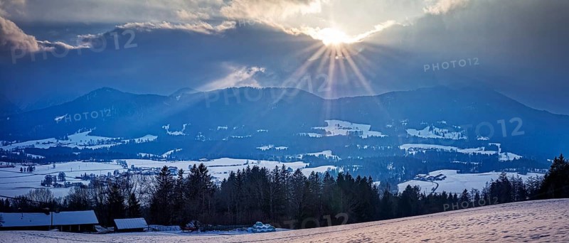 Winter landscape with mountains in the background and sunbeams through the clouds, Fischbachau