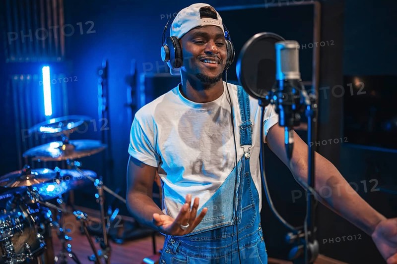 Young, happy african american male artist singing passionately in a professional music recording studio, surrounded by modern equipment and vibrant energy
