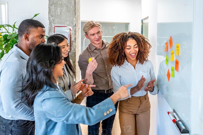 Diverse colleagues brainstorming and planning using colorful sticky notes on a whiteboard, showcasing teamwork and collaboration in a modern office environment