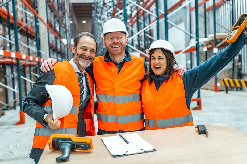 Warehouse workers and their manager are hugging each other, celebrating a successful logistics operation in a large distribution center