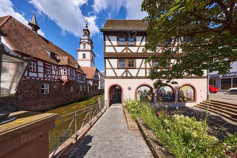 River Mümling, half-timbered houses, archway, church tower, lantern, metal railing, flower bed, blue sky with cumulus clouds, main street, Erbach, Odenwald, Odenwaldkreis, Hesse, Germany, Europe