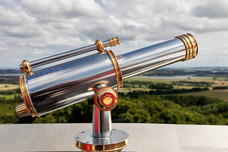 Metallic telescope points into the distance over a vast landscape under a cloudy sky, Rügen, Granitz Castle