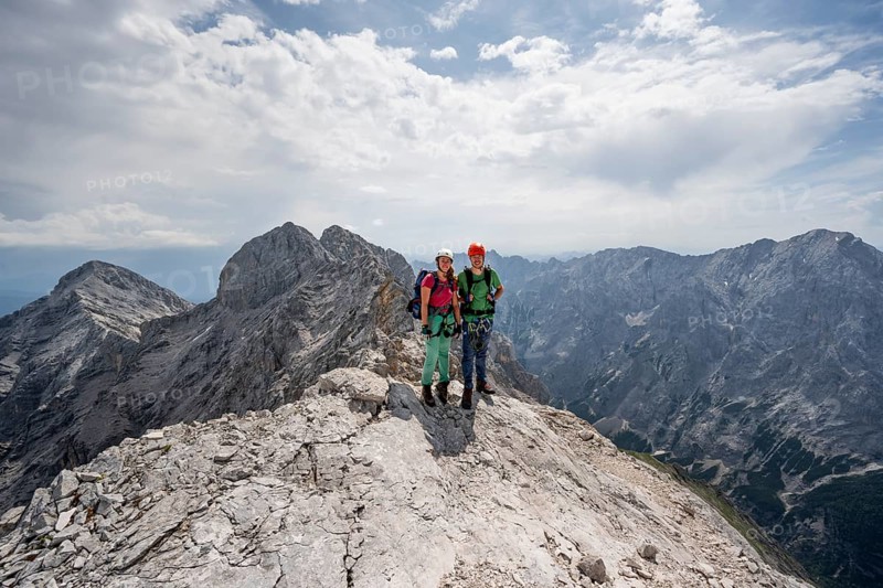 Couple, two mountaineers with helmets on a narrow rocky ridge, crossing the Jubiläumsgrat, view of rocky mountain peaks and Alpspitze, Wetterstein range, Bavaria, Germany, Europe