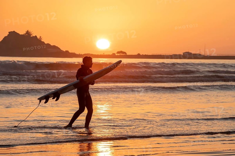 Crescent City, California - A surfer takes his board out of the water as the sun sets over the Pacific Ocean in northern California