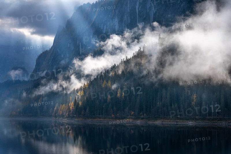 The Vordere Gosausee in autumn with a view of the Gosaukamm. Rays of sunshine shine through the clouds. Forest shrouded in clouds. Vorderer Gosausee, Gosau, Gosau valley, Salzkammergut, Upper Austria, Austria, Europe