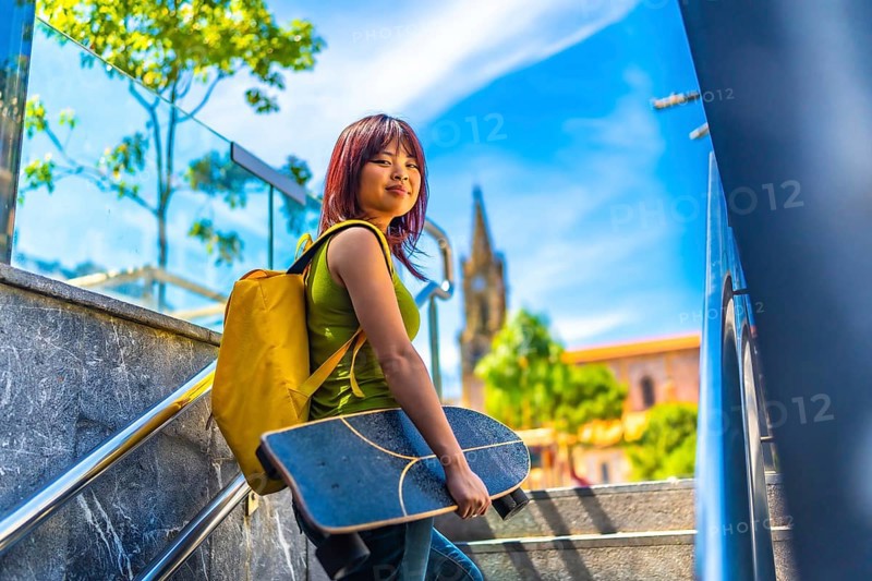 Cool asian young female skater turning to smile at camera walking up stairs in the city