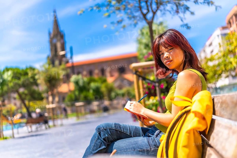 Asian cool young woman sketching sitting on a bench in the city in a sunny day