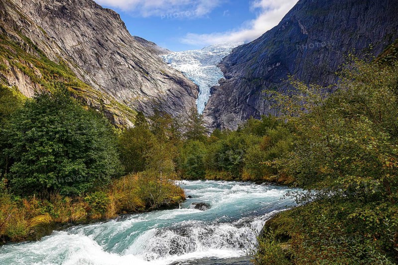River flanked by mountains flows through a green valley with a view of the shimmering Briksdalsbreen glacier in Norway