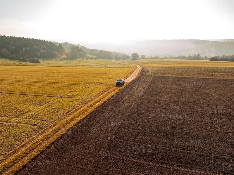 Landscape shot of a car on a path between golden and brown fields in sunlight, electric car VW ID5, Deer Carsharing, Gechingen, Black Forest, Germany, Europe