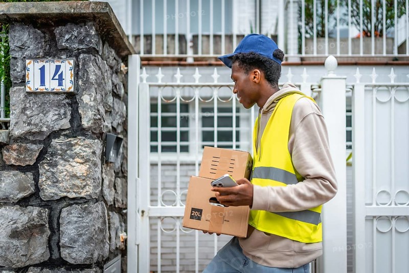 African delivery man arriving on the entrance of a house carrying some packages to deliver