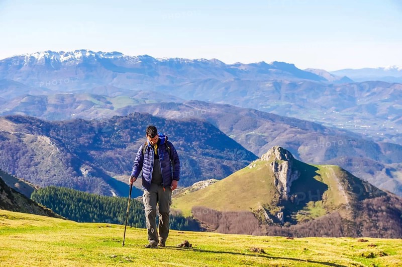 Male hiker walking on a grassy mountain slope with scenic views of the pyrenees mountains in the background