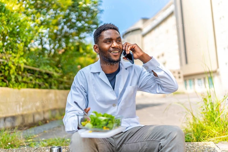 African doctor talking to the phone during lunch break sitting outside the hospital