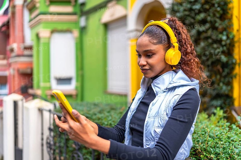 African american woman using phone while listening to music standing in a colorful street