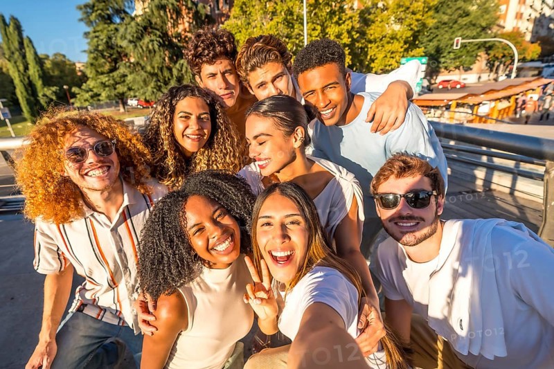 Multi-ethnic young casual and happy friends gesturing success while taking selfie in the city street