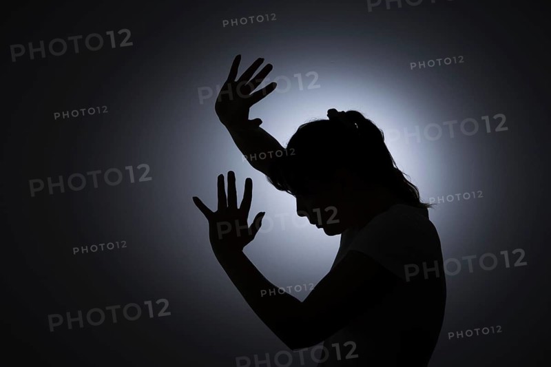 Symbolic photo on the subject of violence against woman. The silhouette of a young woman with her hands held protectively in front of her face is silhouetted against a white wall. Berlin, 22 August 2024
